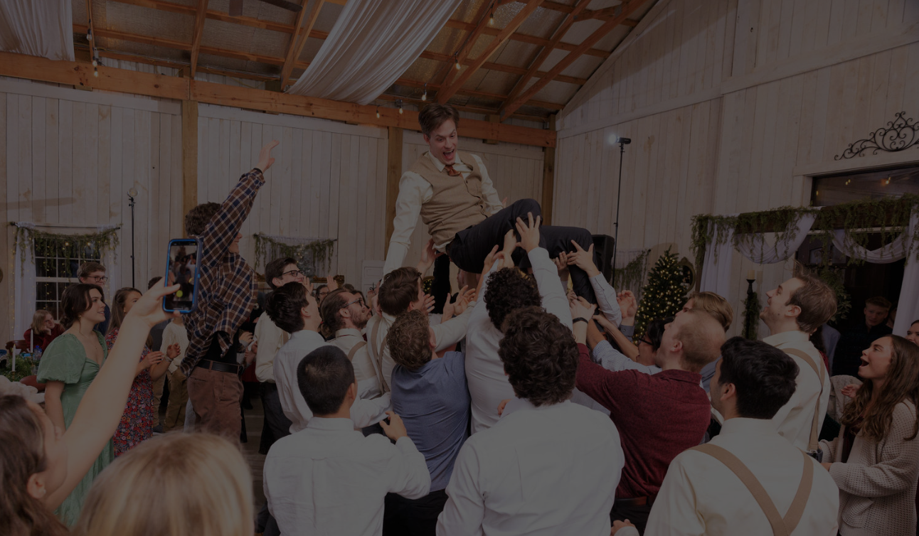 Groom is held up by his friends and family at wedding reception